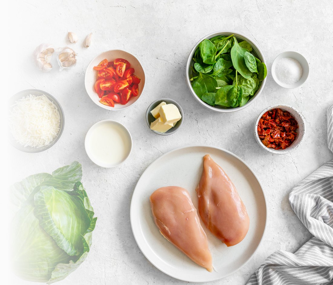 Chicken breasts, spinach, tomatoes, cheese and butter laid out on a pale worktop