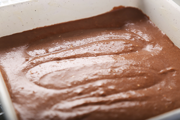 Chocolate brownie batter spread evenly in a white baking pan with swirl marks on top