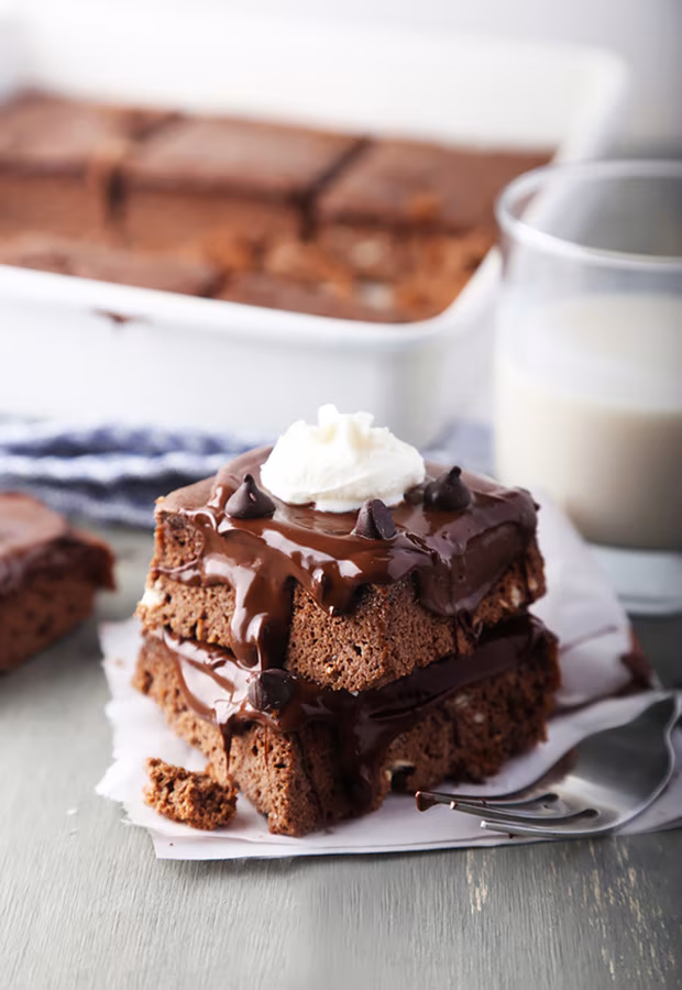 Stacked keto brownies topped with chocolate ganache, chocolate chips, and whipped cream