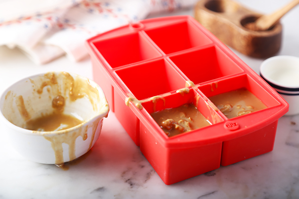 Peanut butter spooned into two wells of a red silicone mold tray