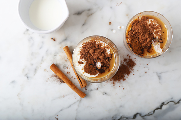 Dark cocoa powder and allspice added to peanut butter mixture in small glass cups on marble