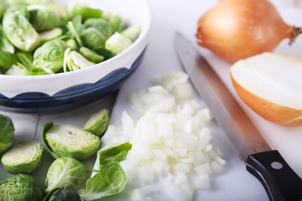 Finely diced onion on a cutting board with halved Brussels sprouts in a bowl