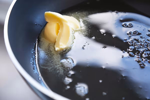 Butter melting into bacon fat in the pan with golden grease surrounding it