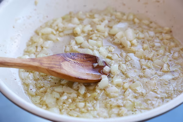 Diced onion and minced garlic sauteing in browned butter in a white pan