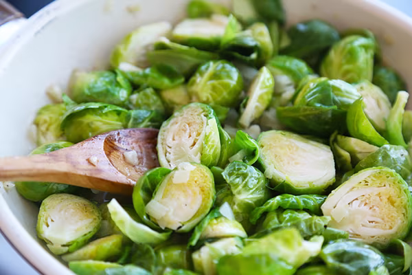 Stirring halved Brussels sprouts into the garlic and onion mixture with a wooden spoon
