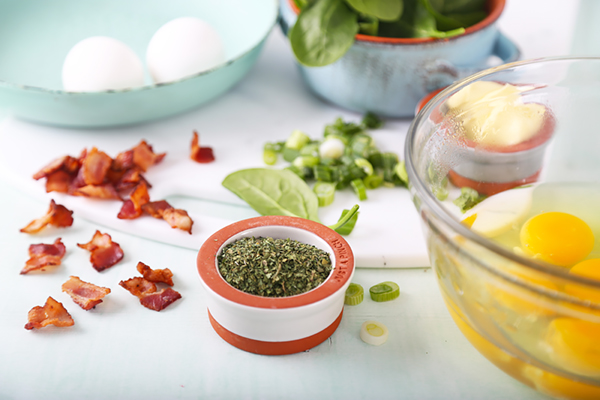 Chopped bacon, dried parsley, sliced green onions, spinach, and cracked eggs on a cutting board