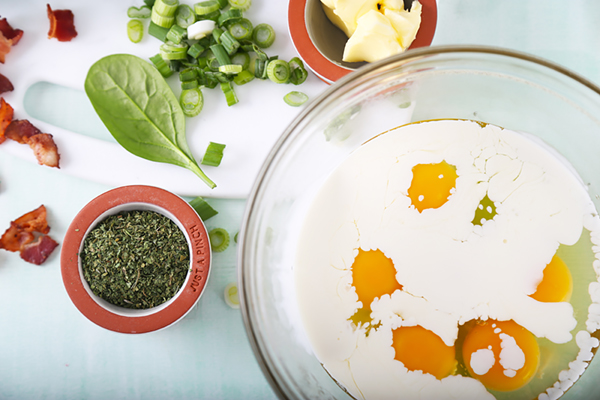 Raw eggs floating in half-and-half in a glass bowl with bright yellow yolks unmixed