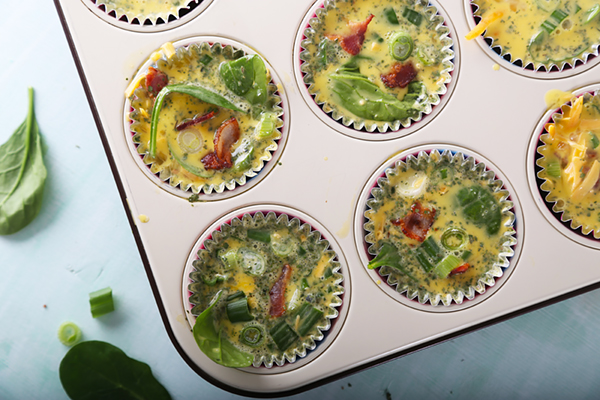 Bacon frittata mixture filling paper-lined muffin tin cups with spinach and bacon visible
