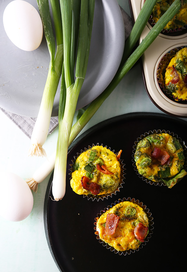 Three baked bacon and cheddar frittata cups with parsley on a black plate