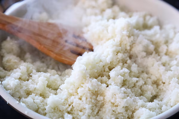 Steaming riced cauliflower in a saucepan stirred with a wooden spoon