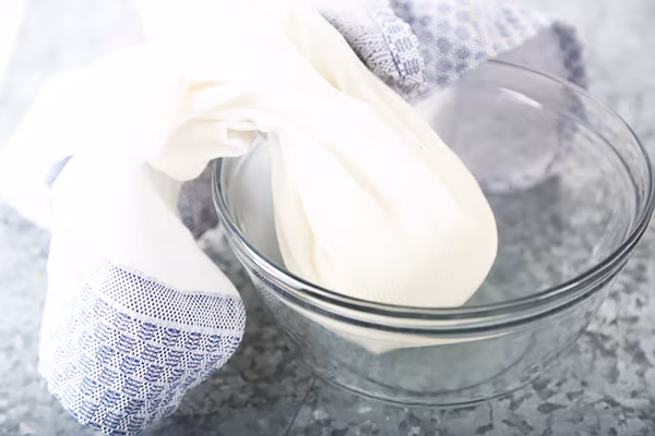 Cooked cauliflower wrapped in a kitchen towel inside a glass bowl for wringing