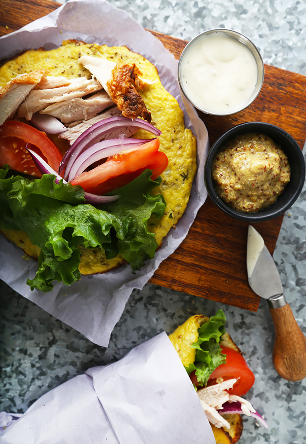 Cauliflower wrap filled with sliced chicken, lettuce, tomato, and red onion on a board