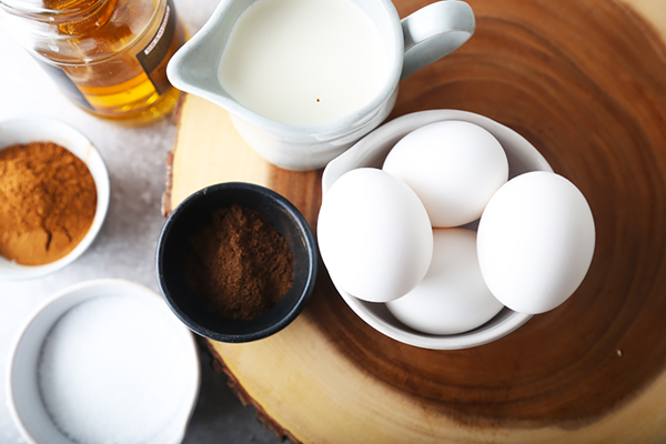 Eggnog ingredients laid out with eggs, heavy cream, rum, cinnamon, and allspice