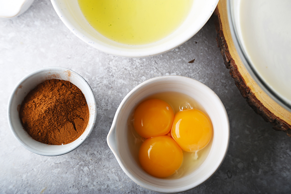 Separated egg yolks and egg whites in small bowls beside ground cinnamon and allspice