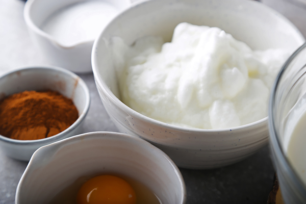 Whipped egg whites with soft peaks in a white bowl next to a reserved whole egg