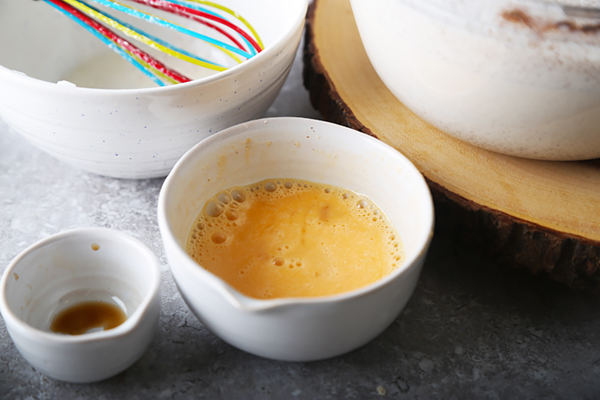 Whisked whole egg in a small bowl next to the finished eggnog and vanilla extract