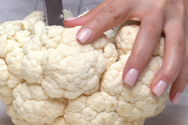 Hand holding a knife against a whole head of cauliflower