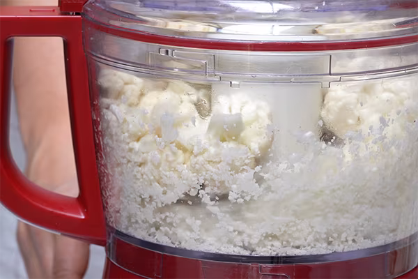Cauliflower florets pulsed into rice-sized pieces inside a red food processor