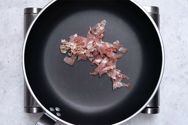 Raw bacon strips placed in a dark nonstick skillet before cooking
