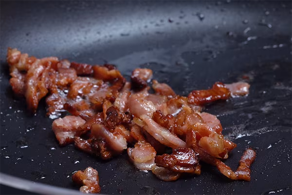 Bacon pieces frying until browned and crispy in a dark skillet