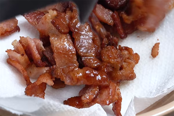 Crispy rendered bacon draining on paper towels after frying