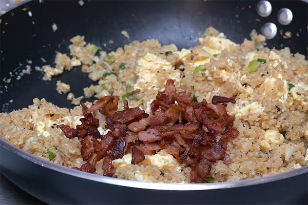 Crispy bacon stirred into finished cauliflower fried rice with egg and green onions