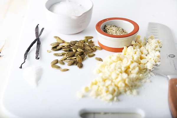 Chopped cocoa butter, toasted pumpkin seeds, hemp seeds, and vanilla bean on a cutting board