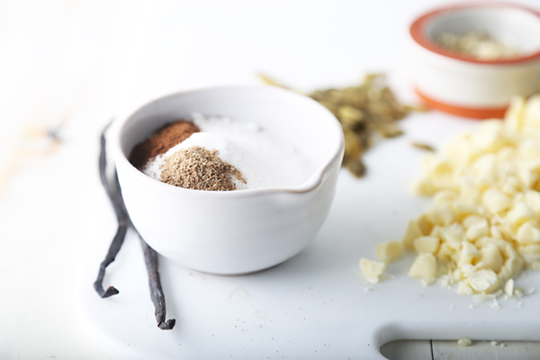 Erythritol and hemp seeds mixed in a small bowl beside chopped cocoa butter and vanilla beans