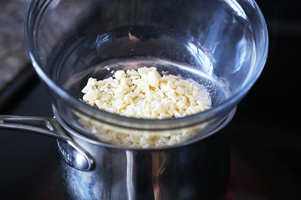 Chopped cocoa butter in a glass bowl set over a saucepan as a double boiler