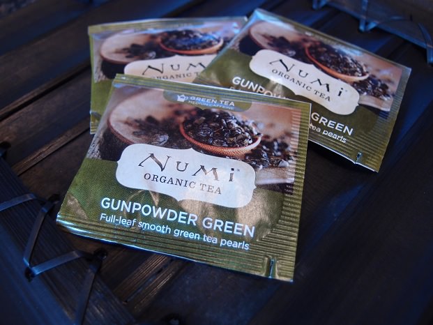 Three packets of organic gunpowder green tea on a dark wooden surface