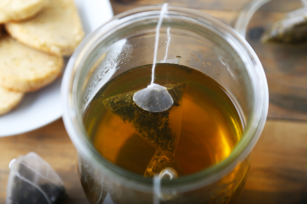 Green tea bag steeping in hot water inside a glass pitcher