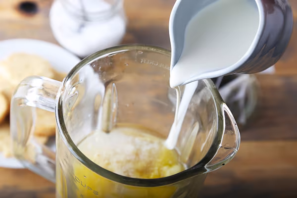 Pouring heavy cream from a small pitcher into the green tea and butter mixture