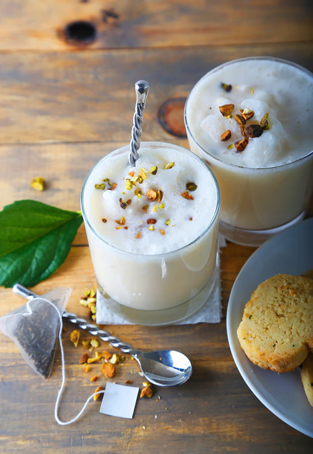 Two glasses of frothy iced ketoproof green tea topped with crushed pistachios on a wooden table