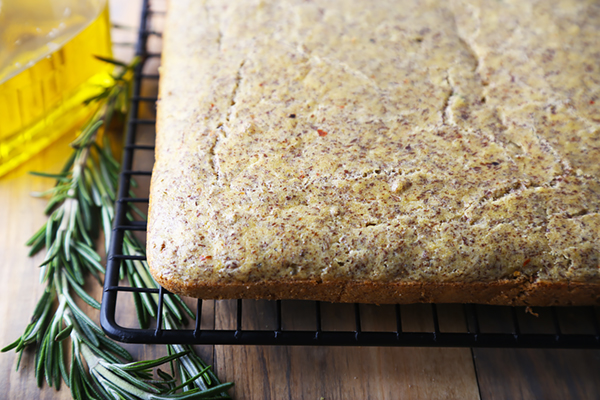 Baked almond flour focaccia cooling on a wire rack with golden top and visible flax specks