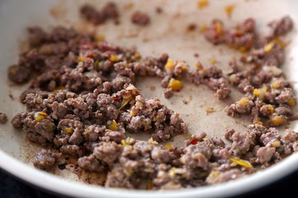 Reserved ground beef mixture browning with diced yellow bell pepper in a skillet