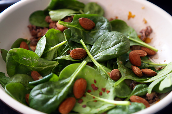 Roasted almonds scattered over baby spinach and ground beef in a skillet