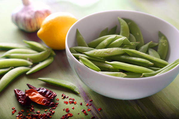 Sugar snap peas in a white bowl with dried red chilies, lemon, and garlic alongside