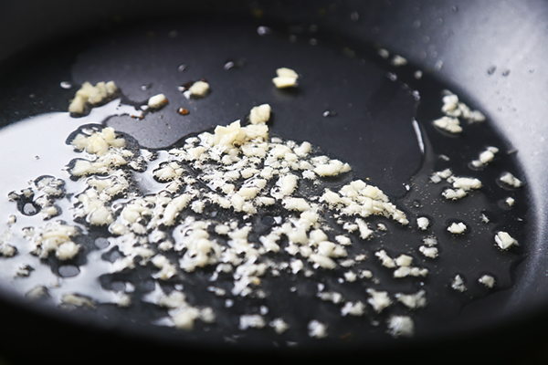 Minced garlic sizzling in hot bacon fat in a dark skillet