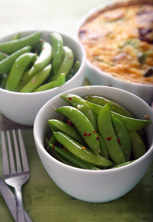 Bacon-infused sugar snap peas sprinkled with red pepper flakes served in two white bowls