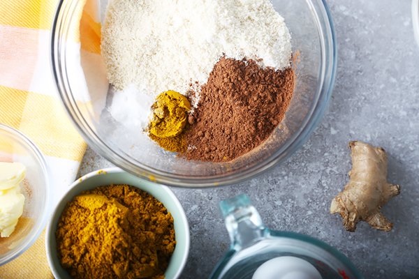 Almond flour, cocoa powder, curry powder, and salt measured into a glass bowl with fresh ginger
