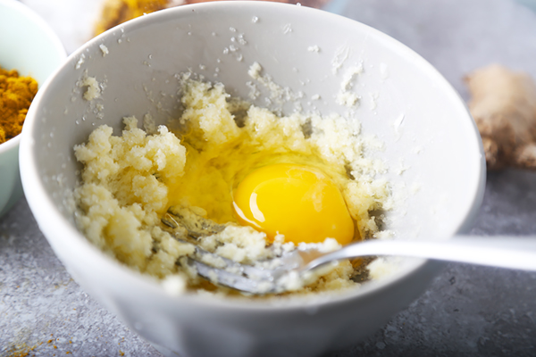 Raw egg cracked into the creamed butter and erythritol in a white bowl