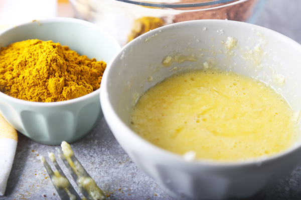 Beaten egg and butter mixture in a white bowl next to curry powder