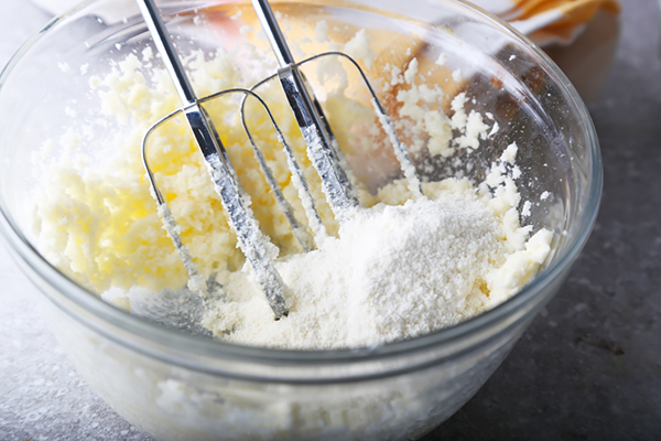 Beating powdered erythritol into butter with a hand mixer in a glass bowl