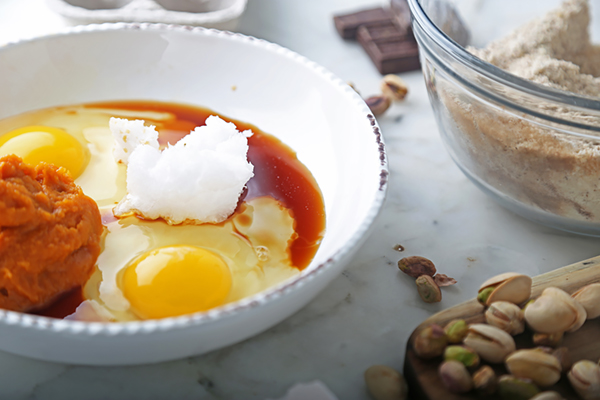 Pumpkin puree, eggs, coconut oil, and vanilla extract in a white bowl before mixing