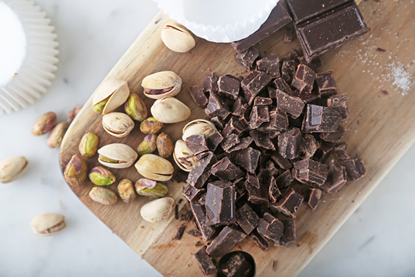 Roughly chopped dark chocolate chunks and whole pistachios on a wooden cutting board