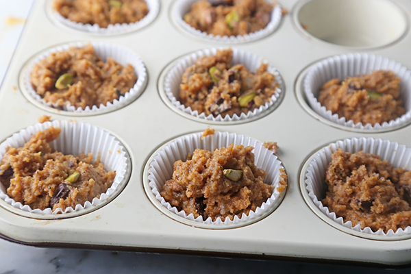 Pumpkin muffin batter portioned into paper-lined muffin tin cups with visible pistachio pieces