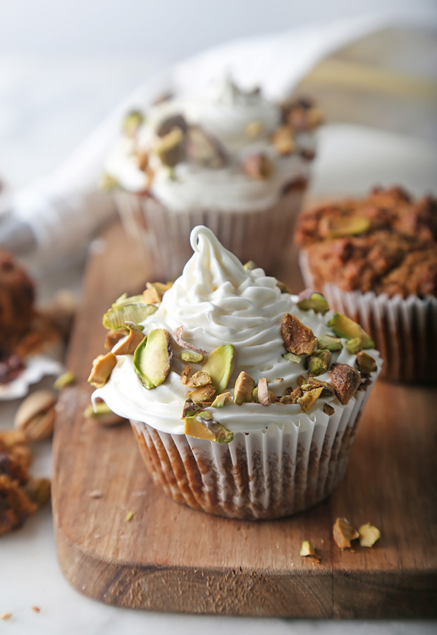 Spiced pumpkin muffins topped with swirled whipped cream and crushed pistachios on a wooden board