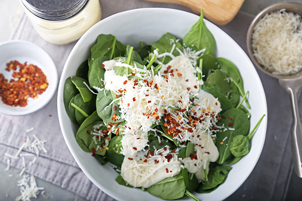 Ranch dressing, shredded parmesan, and red pepper flakes over fresh spinach in a white bowl