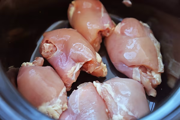 Raw boneless chicken thighs arranged in a slow cooker before adding sauce