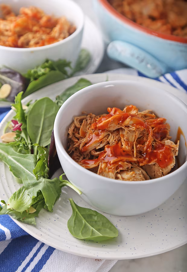 Shredded BBQ pulled chicken in a white bowl with mixed greens on the side